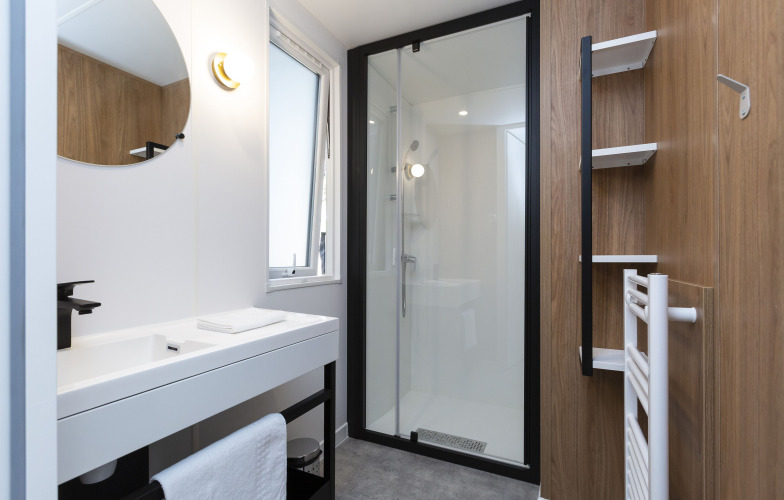 Modernes Badezimmer in einer Glamping-Unterkunft mit Dusche, weißem Waschbecken und Holzverkleidung.