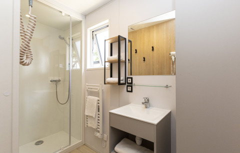 Baño moderno en alojamiento de glamping con ducha, lavabo, espejo y toallas blancas en los estantes.