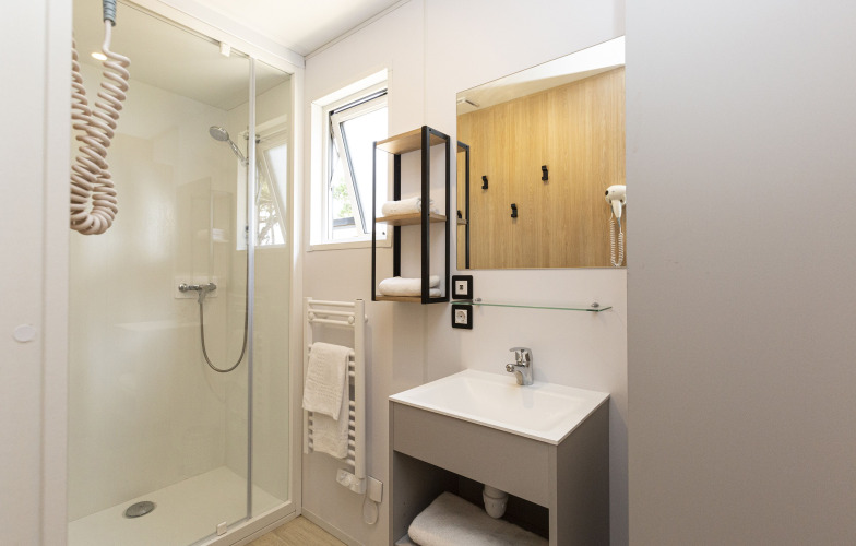 Modernes Badezimmer in einer Glamping-Unterkunft, mit Dusche, Waschbecken, Spiegel und Handtüchern.