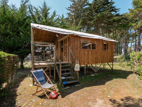 Cabaña de madera elevada con terraza cubierta y silla reclinable, rodeada de árboles en Hut Lodge Standaard.