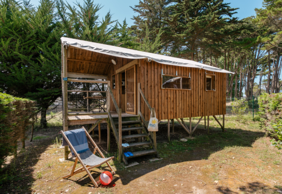 Wooden stilt cabin with covered porch and deck chair outside, surrounded by trees at Hut Lodge Standaard.