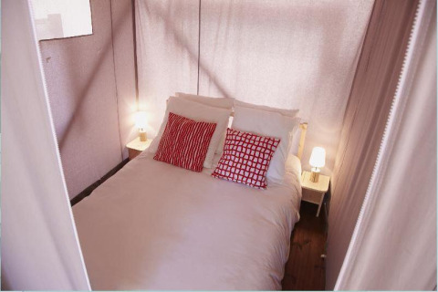 Bedroom in a safari tent at Hut Lodge Standaard, Flower Camping Le Bois d'Amour, France with red pillows.