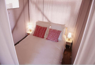 Bedroom in a safari tent at Hut Lodge Standaard, Flower Camping Le Bois d'Amour, France with red pillows.