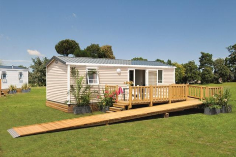 Modern glamping-verblijf met houten terras en oprit op een grasveld onder een heldere blauwe lucht.