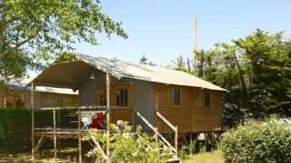 Safari telt kaldet Hut Lodge Comfort med træterrasse og have, omgivet af grønne træer og buske.