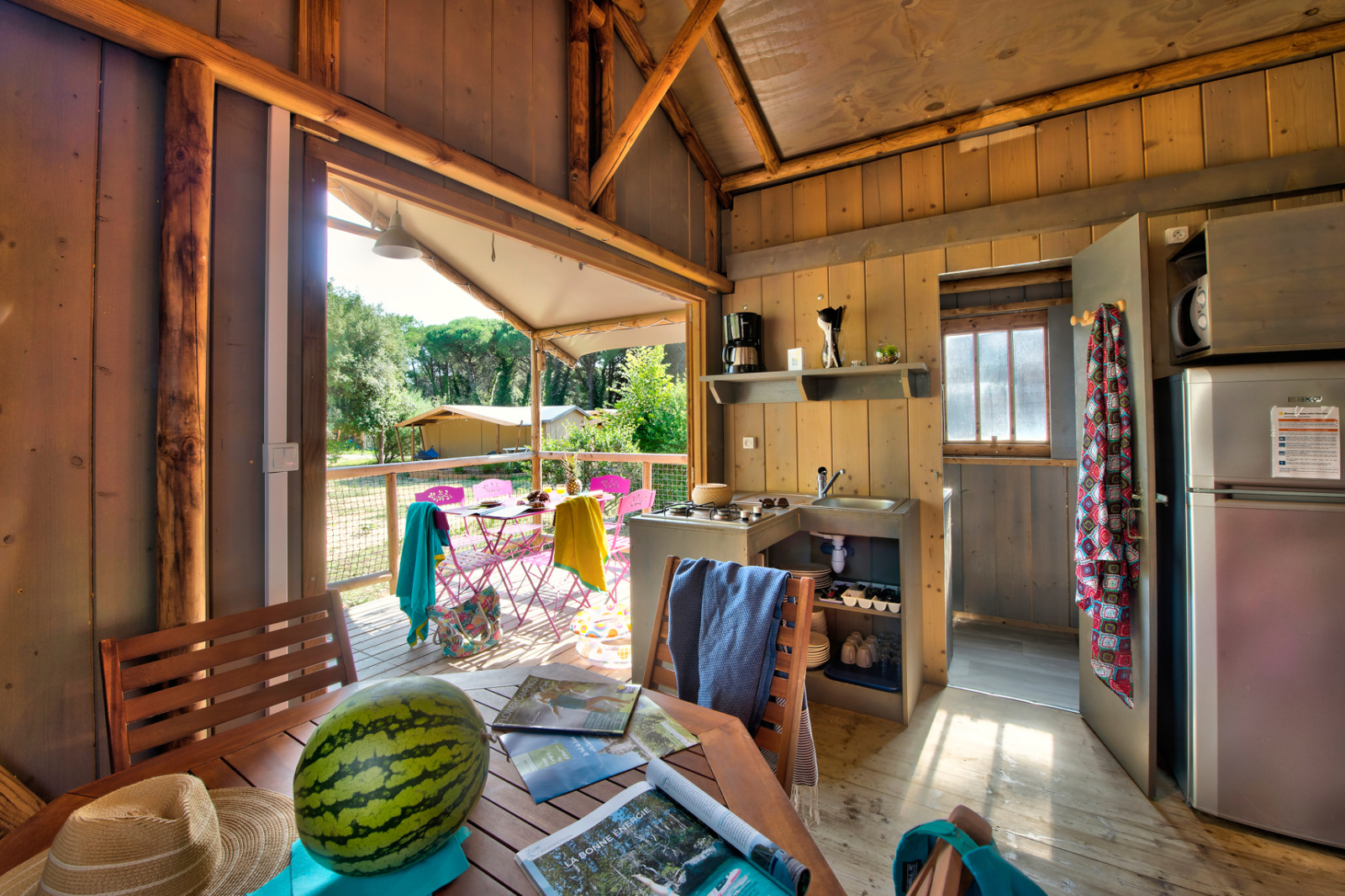 Interieur van een comfortabele safaritent met houten panelen, keuken en buitenterras op een Franse camping.