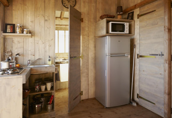 Coin cuisine sous tente safari avec gazinière, évier, réfrigérateur et micro-ondes au Bois d'Amour, France.