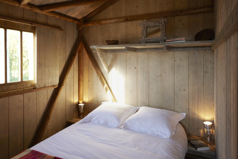 Soveværelse med træpaneler, dobbeltseng og hyggelig belysning i Hut Lodge Comfort, Flower Camping Le Bois d'Amour.