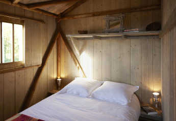 Soveværelse med træpaneler, dobbeltseng og hyggelig belysning i Hut Lodge Comfort, Flower Camping Le Bois d'Amour.
