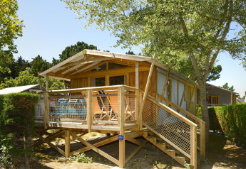 Das Safari-Zelt Hut Sweetflower Premium mit erhöhter Holzterrasse, umgeben von Bäumen und Büschen.