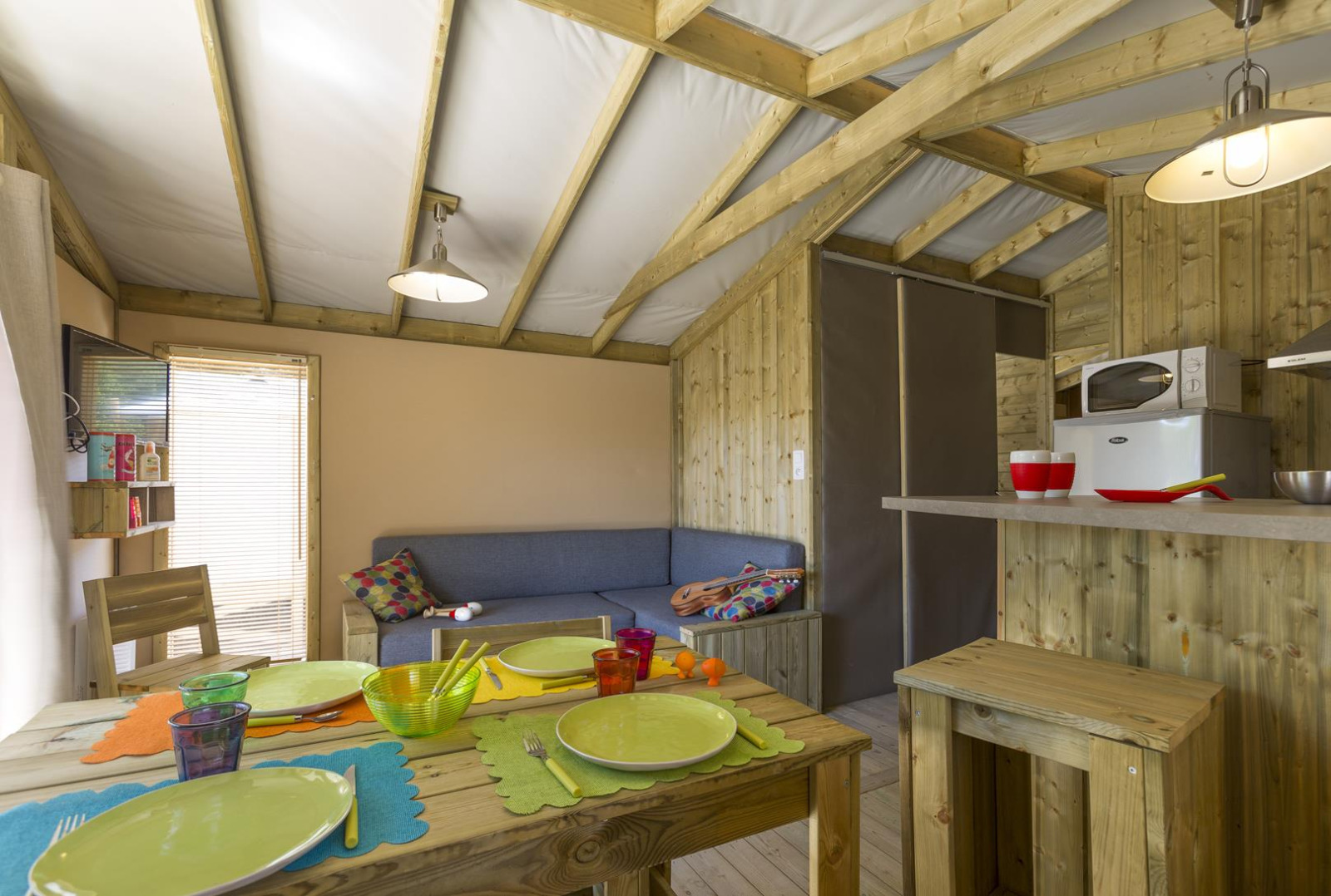 Interieur van een gezellige safaritent met houten wanden, eettafel, bank en keukenblok in Frankrijk.
