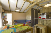 Interior de una acogedora tienda safari con paredes de madera, mesa de comedor, sofá y cocina en Francia.