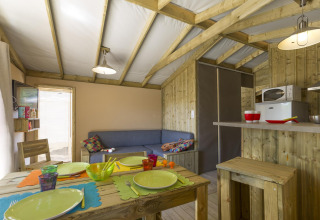 Interno di una tenda safari accogliente con pareti in legno, tavolo da pranzo, divano e angolo cottura in Francia.