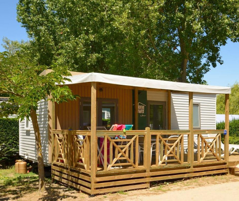 Modern mobile glamping cabin with wooden deck, outdoor seating, and trees for a relaxing retreat.