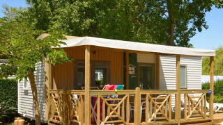Cabaña de glamping móvil con terraza de madera, muebles de exterior y rodeada de vegetación natural.