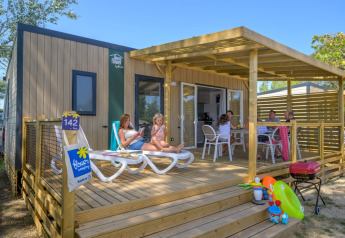 Gezin ontspant op het houten terras van Homeflower Premium lodge met speelgoed en barbecue op de voorgrond.