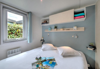 Bright glamping bedroom with a double bed, large window, wall shelves, and cozy modern decoration.