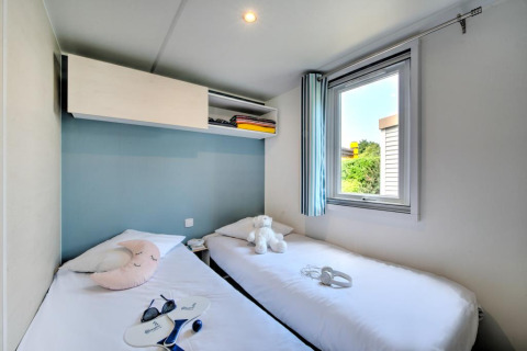 Bright glamping room featuring two single beds, plush toys, a window, and modern storage above the beds.