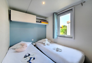Bright glamping room featuring two single beds, plush toys, a window, and modern storage above the beds.