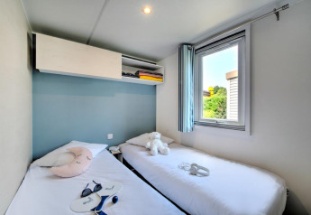 Lichte glampingkamer met twee eenpersoonsbedden, knuffel, raam en moderne opbergruimte boven het bed.