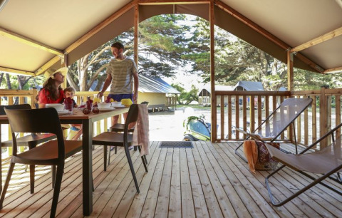 Familie nyder morgenmad i en safariteltslodge på Camping Demoiselles Plage, Frankrig med lys træterrasse.
