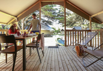 Famiglia fa colazione in una tenda Lodge Confort al Camping Demoiselles Plage, Francia, con terrazza in legno.