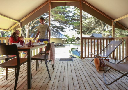 Gezin geniet van ontbijt in een safaritent bij Camping Demoiselles Plage in Frankrijk, houten terras aanwezig.