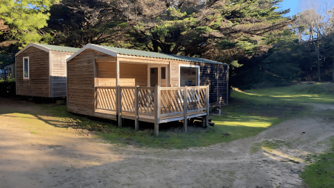 Twee houten chalets bij Stacaravan Confort, omgeven door bomen en zon op een rustige camping.