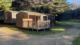 Due cabine di legno allo Stacaravan Confort circondate da alberi e natura in una giornata soleggiata.