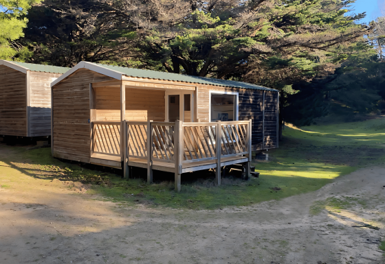 Due cabine di legno allo Stacaravan Confort circondate da alberi e natura in una giornata soleggiata.