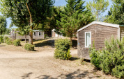 Stacaravan Confort hutten op Camping Demoiselles Plage in Frankrijk, omgeven door bomen en struiken in het zonlicht.