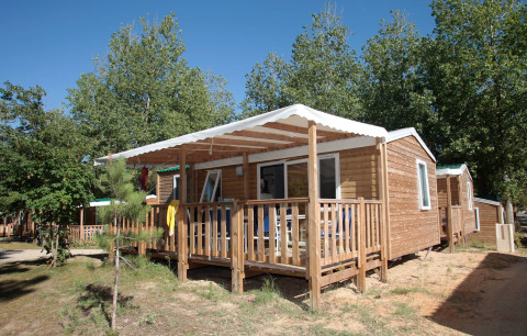 Stacaravan Confort cabin with wooden porch and white canopy, surrounded by trees on a sunny day
