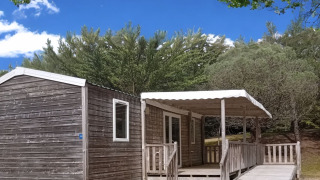 Rolstoeltoegankelijke houten stacaravan met oprijplaat en overdekte veranda, omringd door natuur.