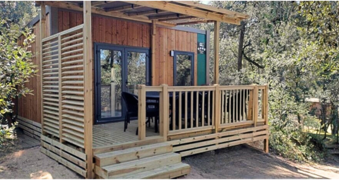 Buitenaanzicht van de Homeflower Premium 1 kamer lodge met houten terras en omringd door groen en bomen.