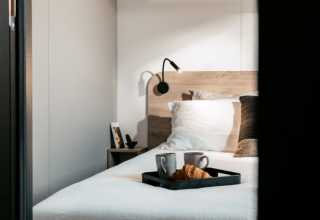 Gezellige slaapkamer met ontbijtplank op bed bij Homeflower Premium 1 kamer in Flower Camping Les Dunes, Frankrijk.