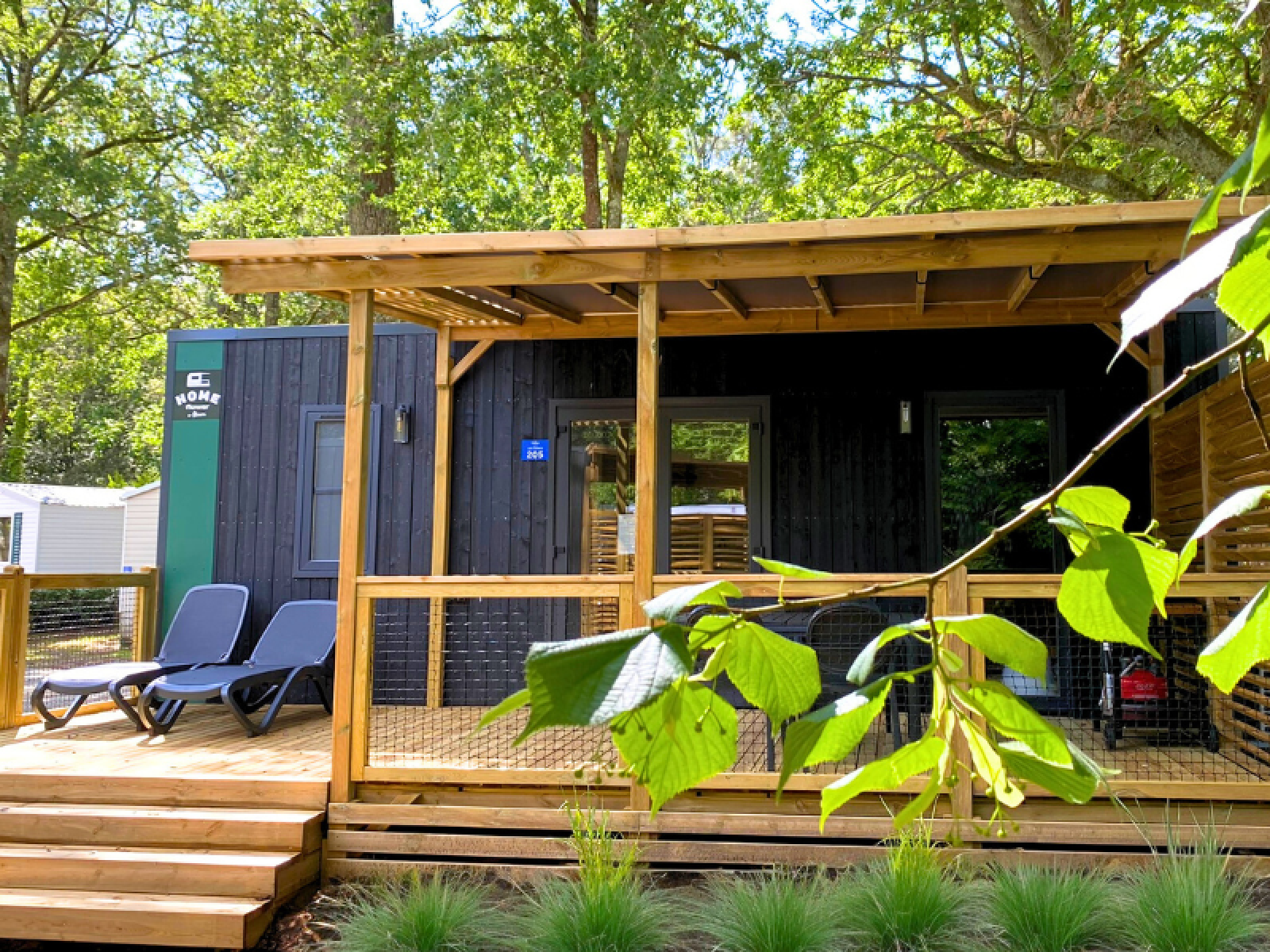 Glampingaccommodatie met houten veranda, ligstoelen en veel groen in een bosrijke omgeving.