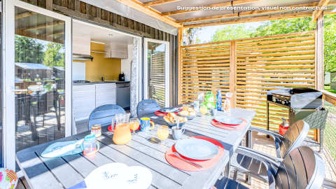 Buiten eetgedeelte bij glampingaccommodatie, gedekte tafel met eten en drinken op zonnig terras met barbecue.