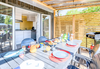 Outdoor dining at a glamping accommodation, set table with food and drinks on a sunny terrace with a grill.