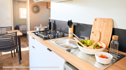 Coin cuisine moderne en glamping avec gazinière, évier, salade fraîche et table à manger lumineuse.