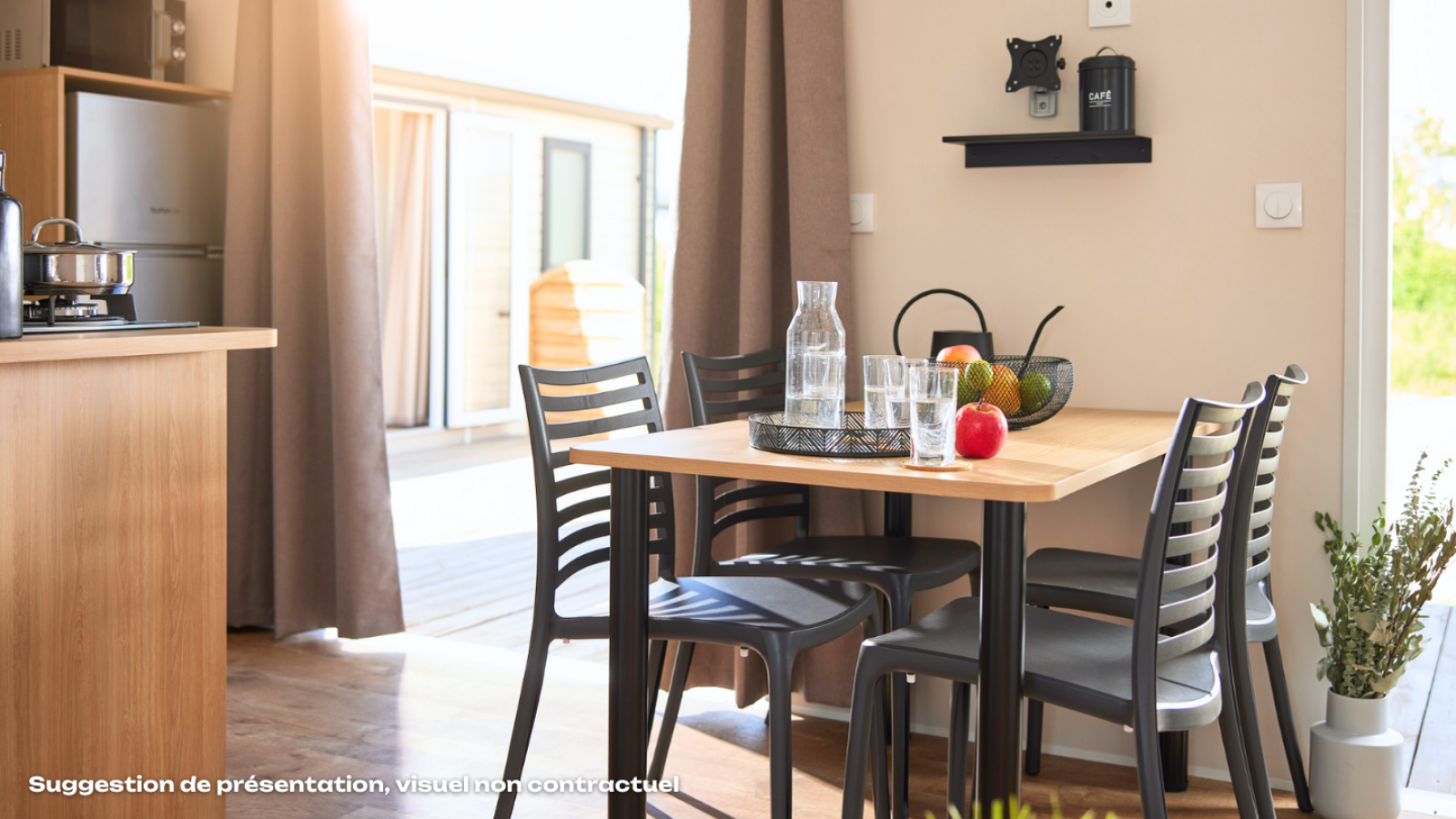 Lichte glamping eetruimte met houten tafel, zwarte stoelen, fruit, glazen en uitzicht op het terras.