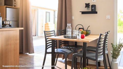 Bright glamping kitchen and dining area with wooden table, black chairs, fruit, and sunlit terrace view.