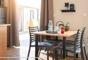 Lichte glamping eetkamer met houten tafel, zwarte stoelen, fruitmand, glazen en zicht op terras.