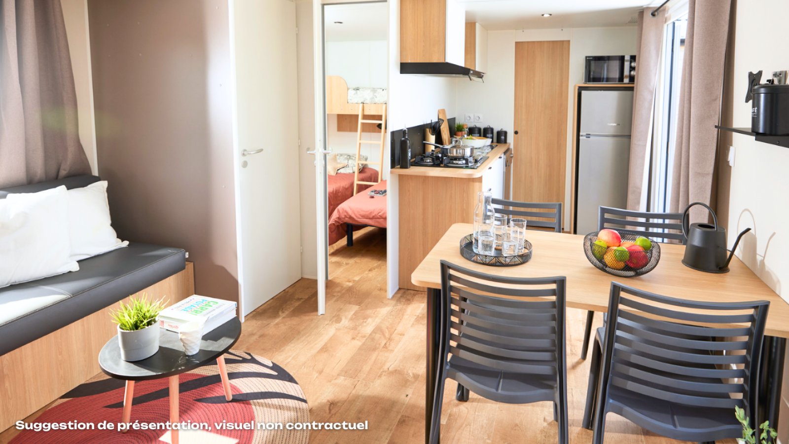 Moderne glampingaccommodatie met eettafel, keuken, zithoek en slaapkamer met stapelbed op de achtergrond.