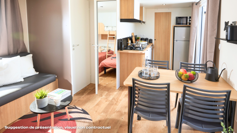 Alojamiento glamping moderno con mesa de comedor, sofá, cocina y dormitorio con literas al fondo.