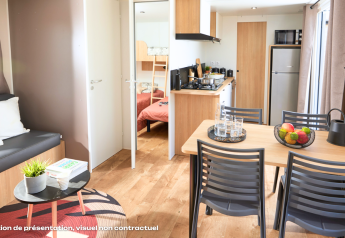 Alojamiento glamping moderno con mesa de comedor, sofá, cocina y dormitorio con literas al fondo.