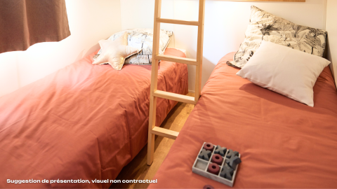 Twee eenpersoonsbedden met perzikkleurig beddengoed in een gezellige glampingruimte met kussens en spel.