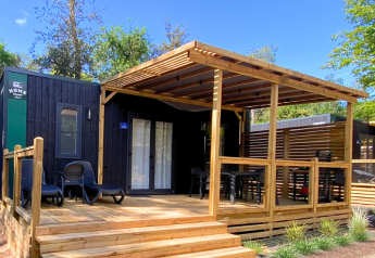 Hébergement glamping moderne avec façade noire, grande terrasse en bois et coin salon ombragé.