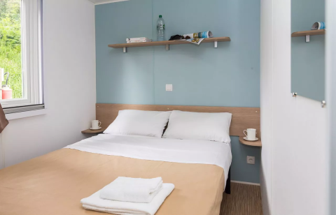 Cozy glamping room with double bed, soft linens, a window, shelves, mugs, and a calming blue wall.