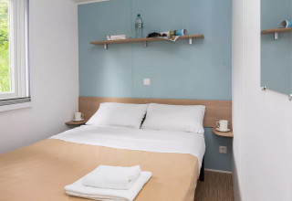 Accogliente camera glamping con letto matrimoniale, lenzuola bianche, scaffale, finestra e tazze.