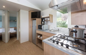 Cuisine de glamping moderne avec gazinière, casserole, frigo, micro-ondes et vue sur chambre et extérieur.